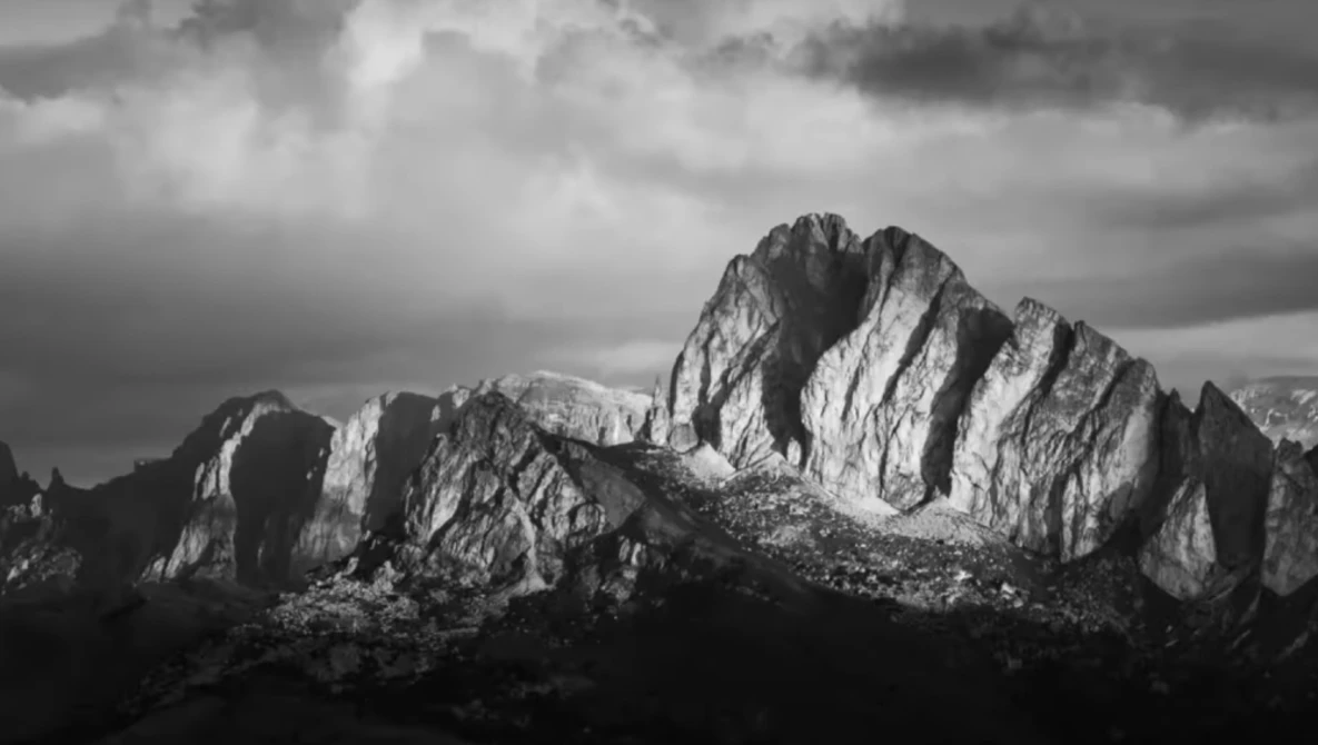 Dramatic black and white mountain landscape with jagged peaks and stormy sky overhead.