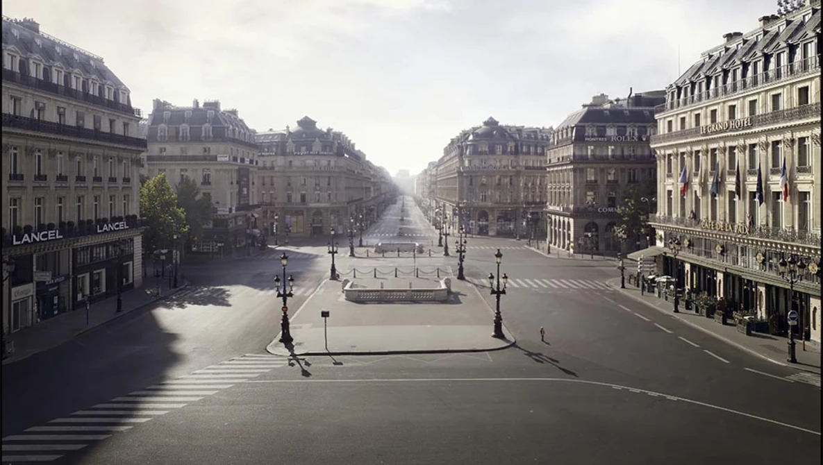 Wide boulevard lined with Haussmann-style buildings, wet pavement reflecting overcast sky, architectural symmetry receding to vanishing point.