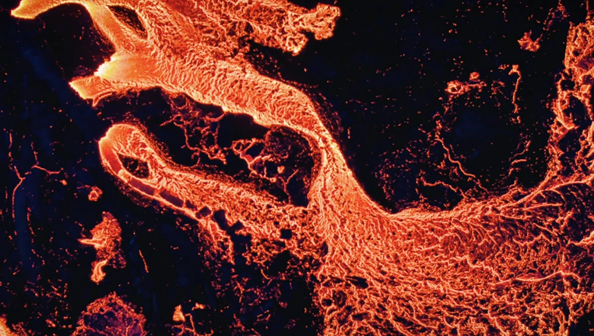 Aerial thermal or infrared view of flowing lava with bright orange and yellow channels against dark cooled rock.