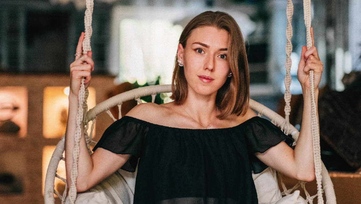 Young woman in black off-shoulder top holding rope swing ropes while looking at camera.