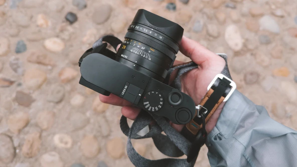 Hand holding a rangefinder camera with a mounted prime lens against a textured stone surface.
