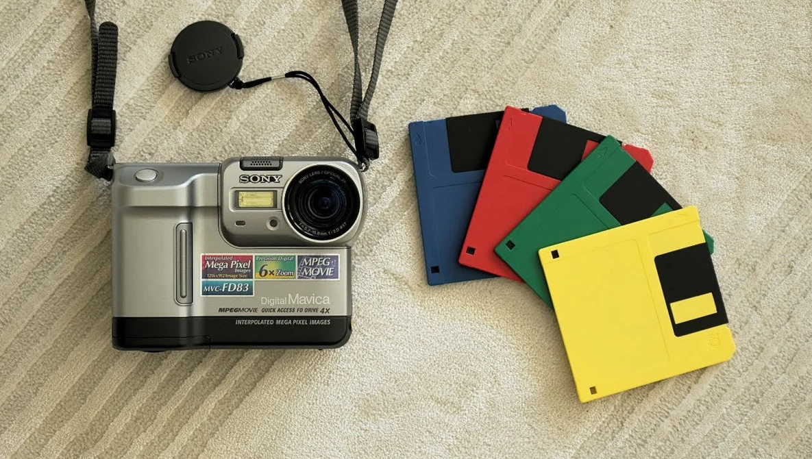 Vintage digital camera with memory cards and lens cap on neutral fabric surface.