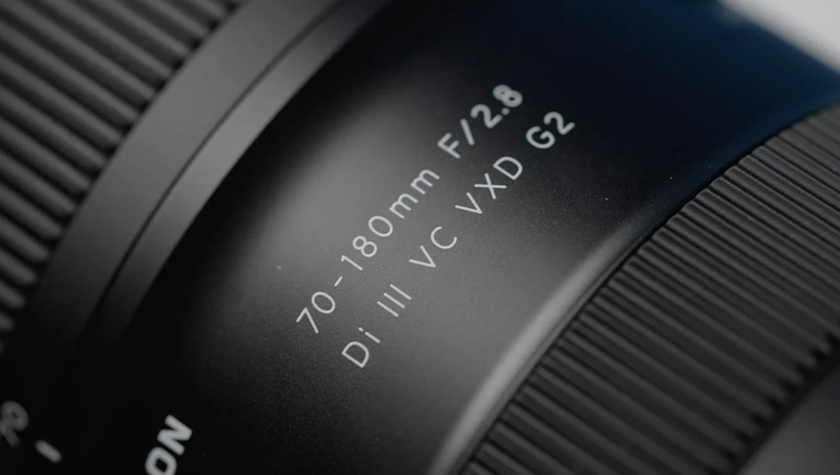 Close-up of camera lens barrel showing 70-180mm focal length and f/2.6 aperture specifications.