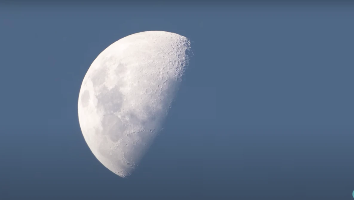 Waning crescent moon against a clear blue sky, surface details and craters visible in sharp focus.