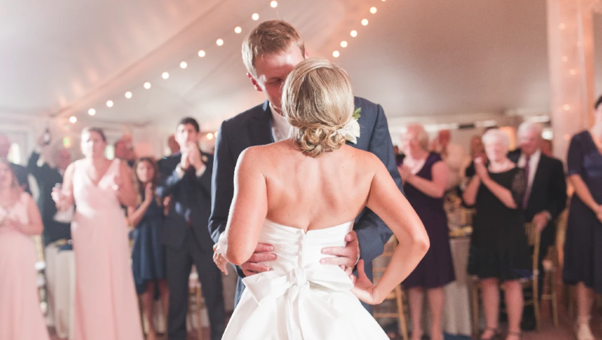Bride and groom dancing during first dance at wedding reception under string lights.