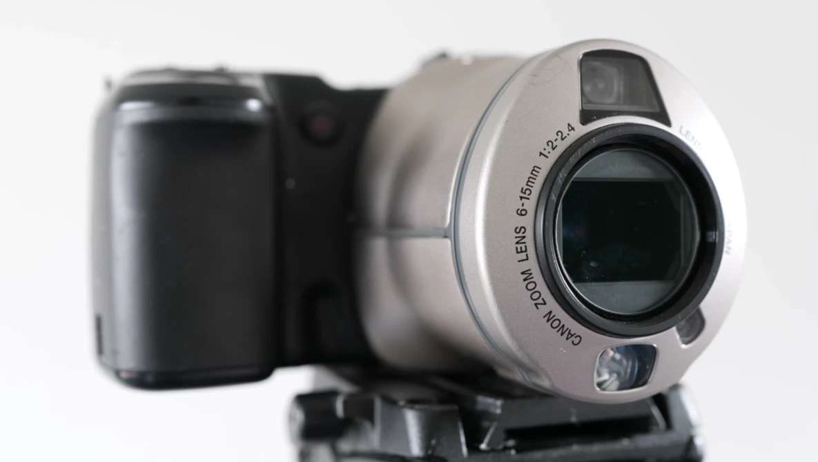 Silver camcorder with black handle shown alongside blurred dark compact camera against white background.