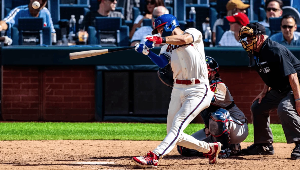 Baseball batter mid-swing during day game with catcher and umpire behind home plate.