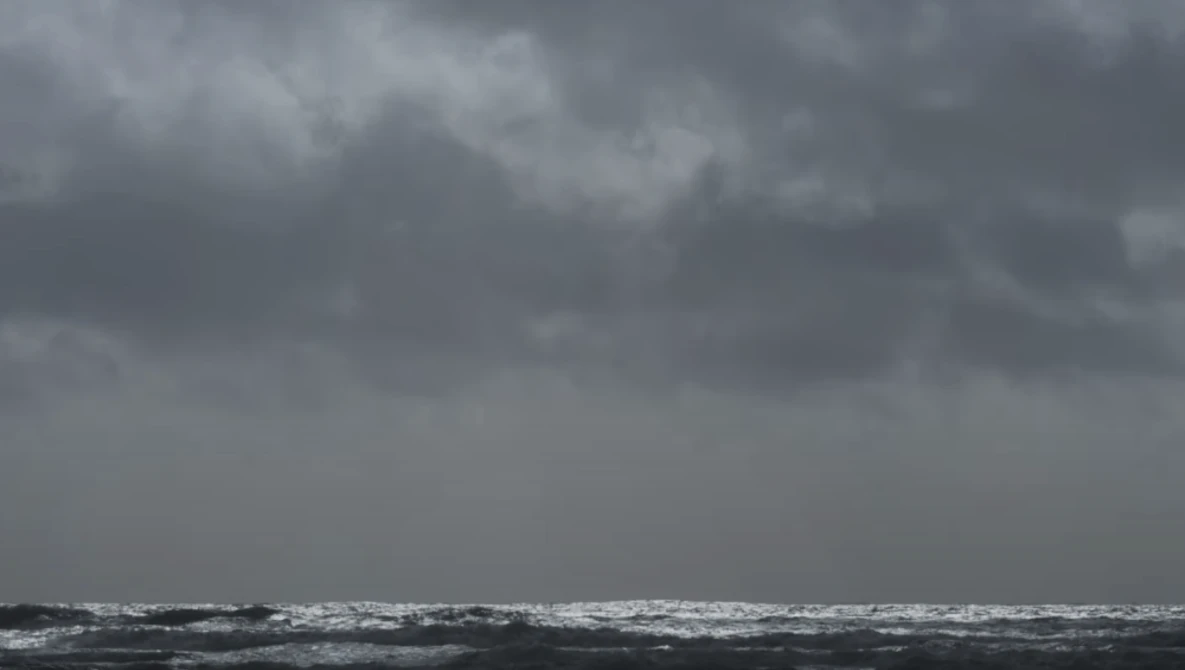 Turbulent ocean waves under heavy gray storm clouds at horizon.