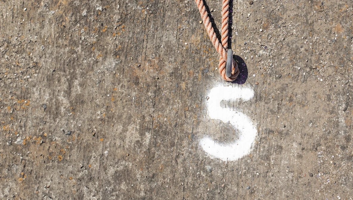White number 5 painted on weathered concrete surface with rope and pulley attached above.