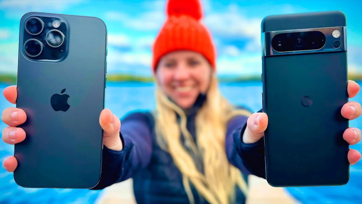 Person holding iPhone 12 Pro and Pixel 6 Pro side by side outdoors with scenic water backdrop.