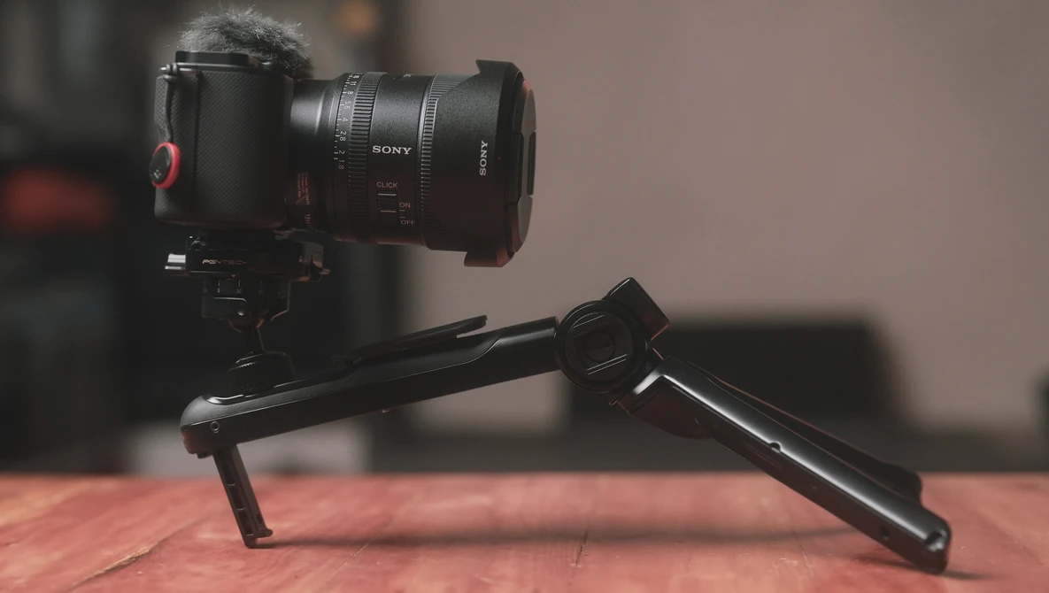 Sony camera with telephoto lens mounted on a black tripod head against a warm-toned backdrop.
