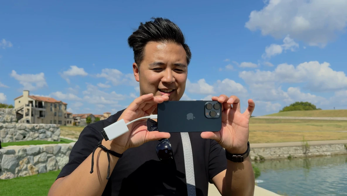 Photographer holding smartphone horizontally to capture landscape scene with water and countryside.