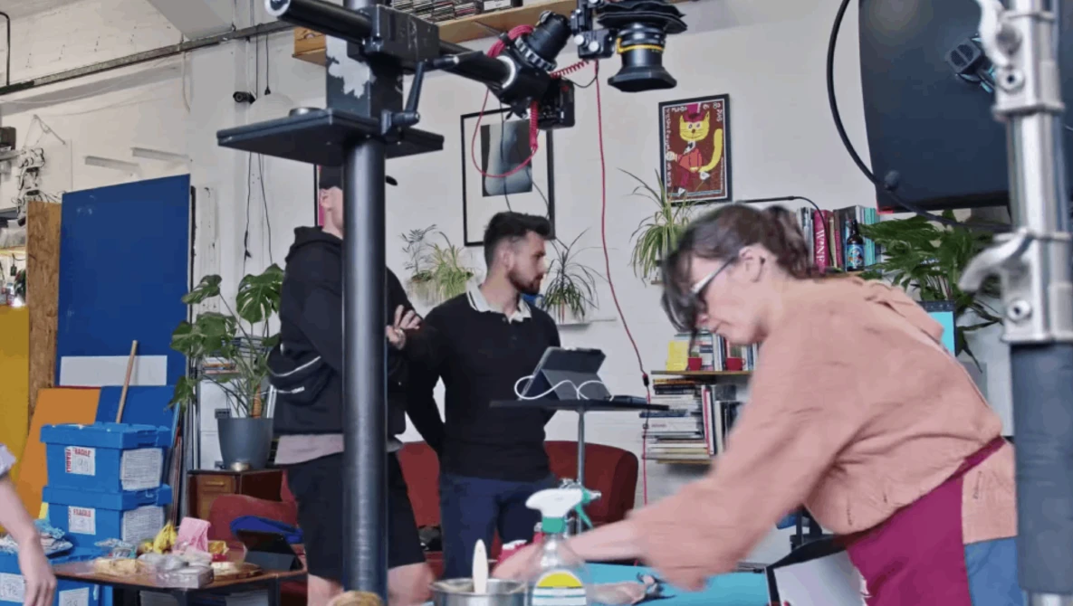 Two people working on a video production set with professional lighting rigs overhead in a creative studio space.