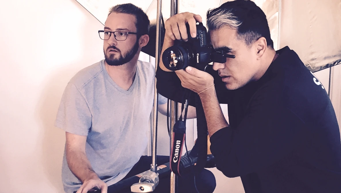 Two photographers examining a Canon camera in a studio setting with white walls and professional lighting.