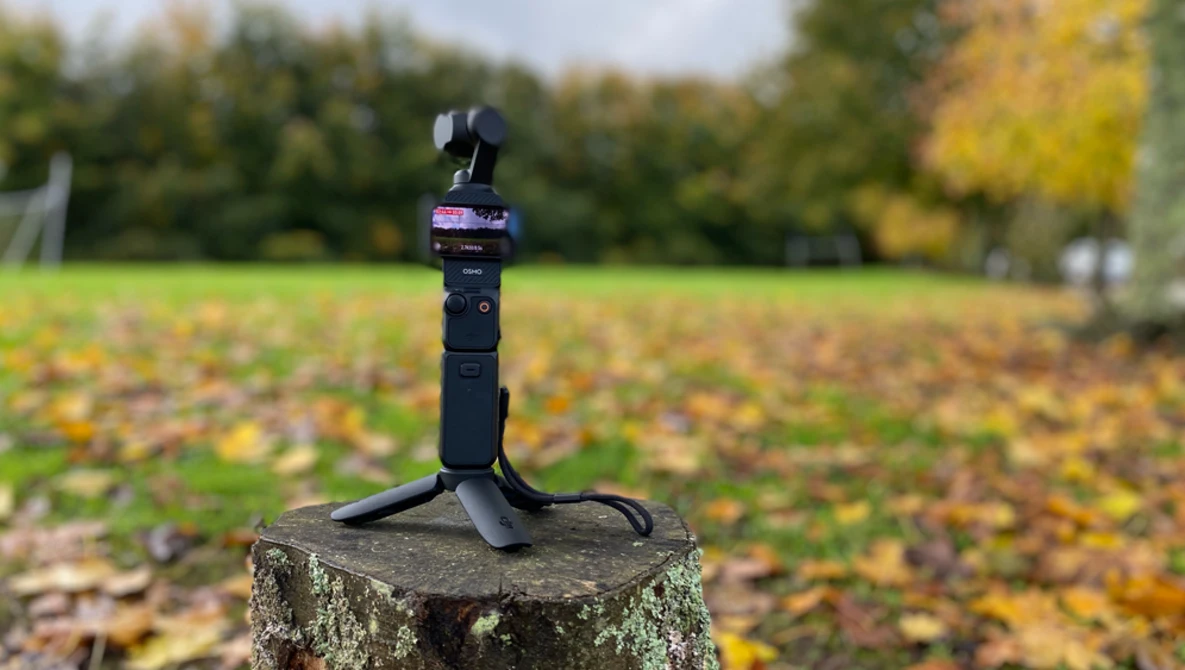 DJI Osmo Pocket camera mounted on a stand in an autumn park setting.