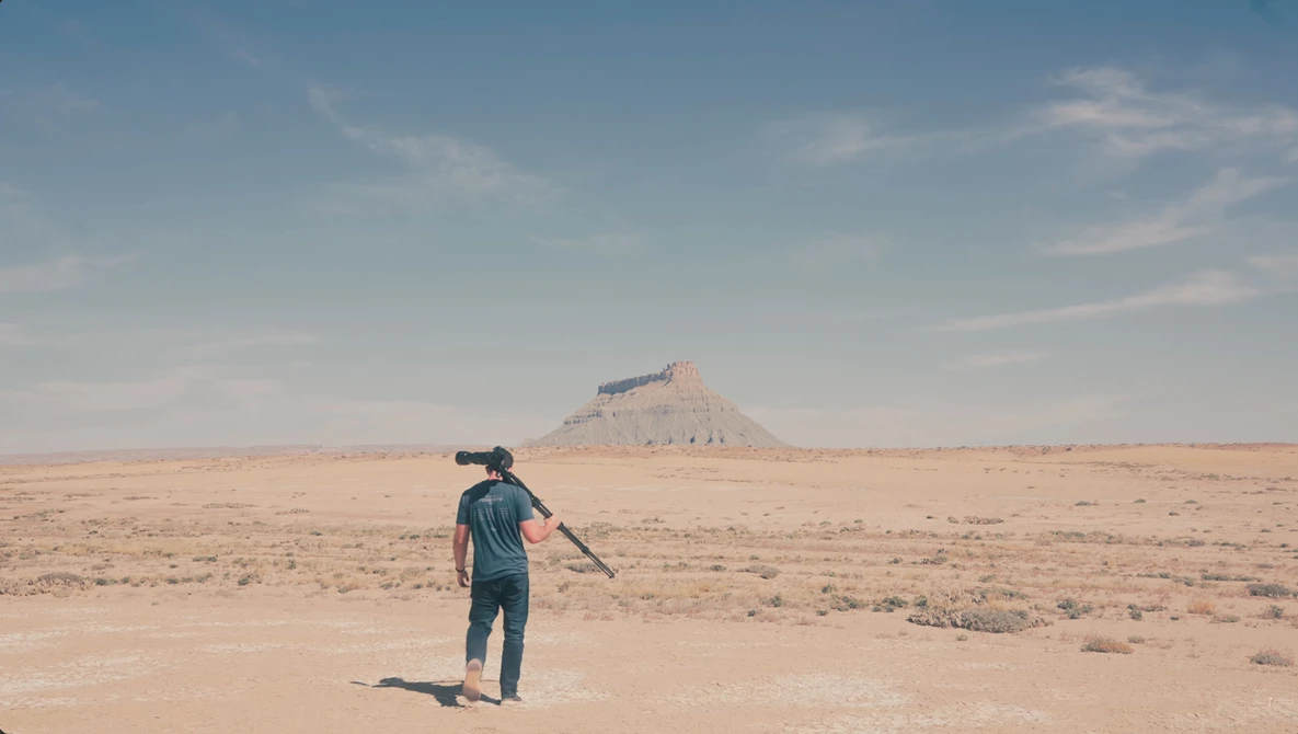 Person standing in vast desert landscape pointing toward distant mountain peak.