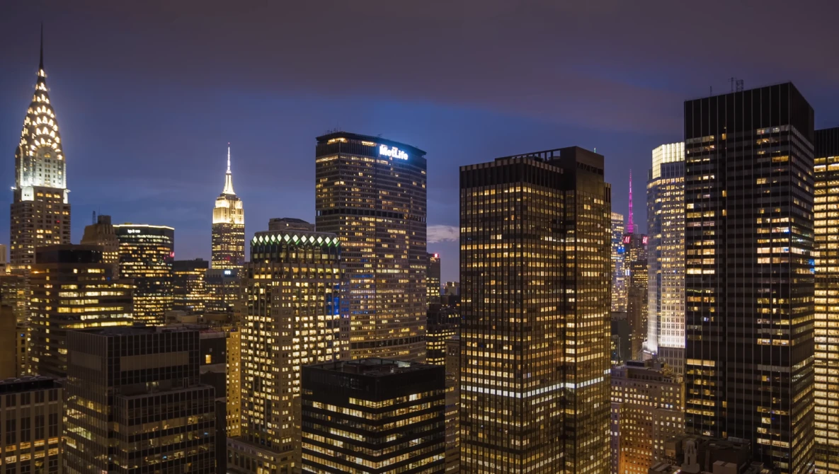 Manhattan skyline at twilight with illuminated skyscrapers including the Chrysler Building and Empire State Building.