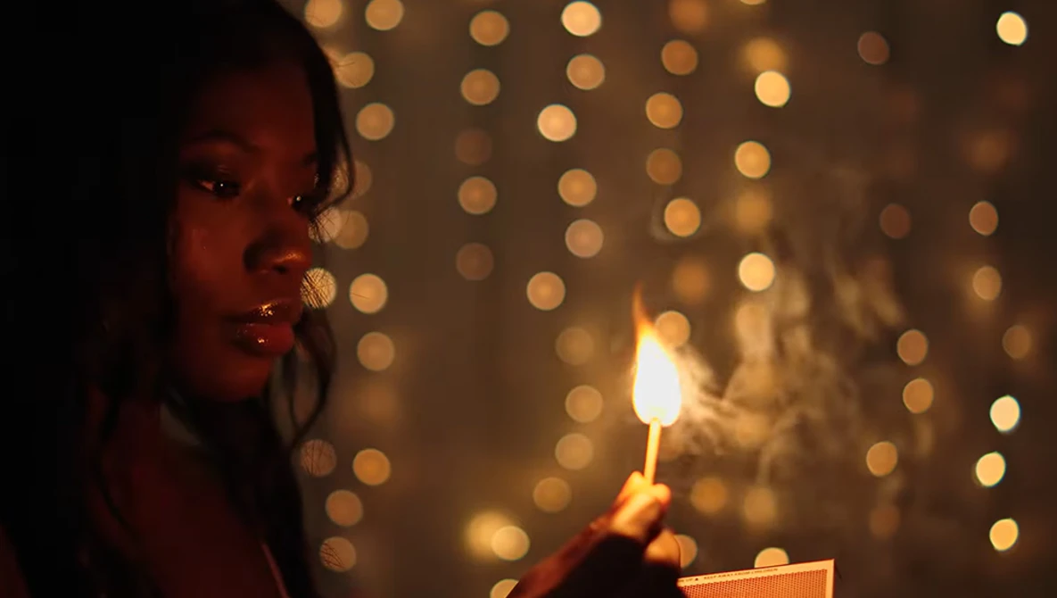 Woman holding a lit candle against a blurred backdrop of warm golden bokeh lights.