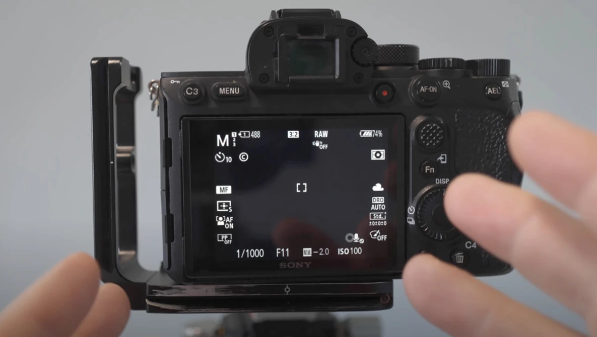 Hands holding a mirrorless camera displaying its rear LCD screen menu and controls.