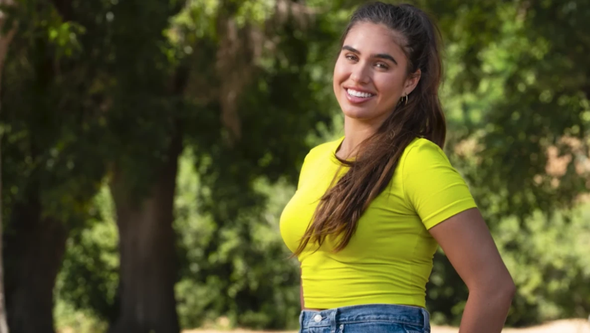 Woman in bright yellow t-shirt smiling at camera with trees in background.