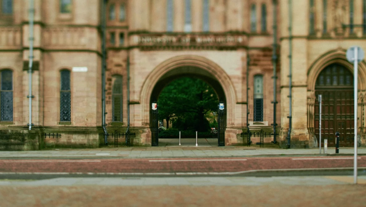 Large arched entrance of a historic stone building with manicured shrubs visible through the opening.