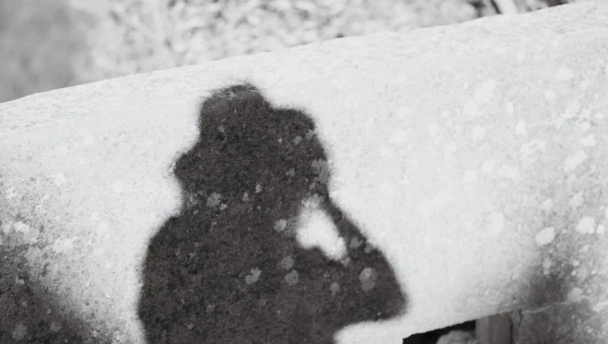 Shadow of a person holding a camera cast on snow-covered surface.