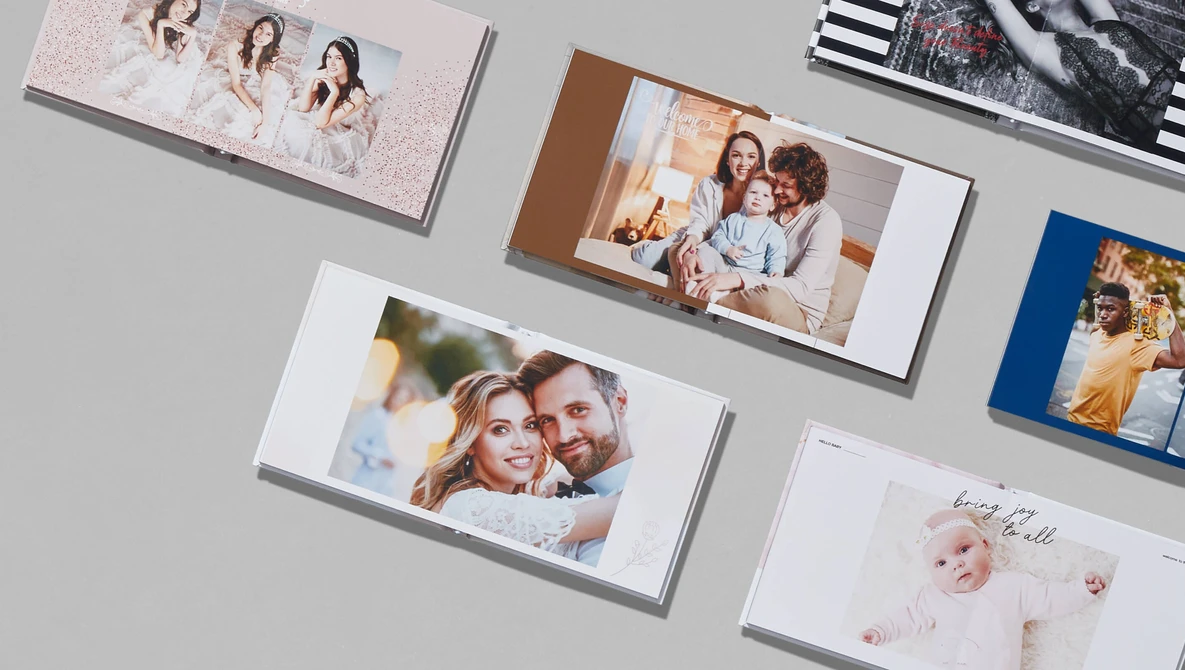 Collection of printed photo books and albums arranged on a gray surface, displaying various family portraits and lifestyle photography.