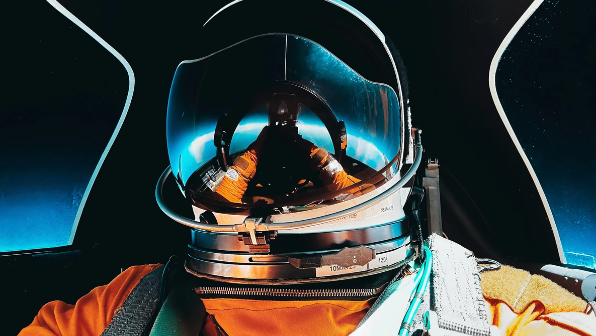 Astronaut in spacesuit with reflective helmet visor showing Earth and spacecraft interior.