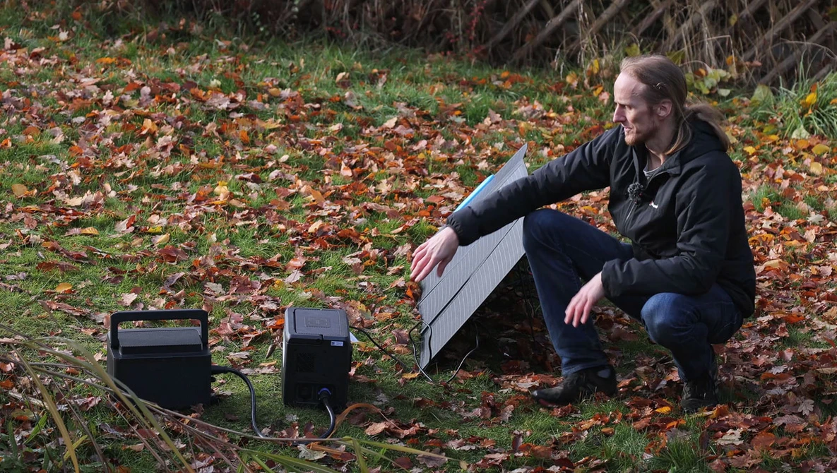 Photographer crouching beside solar panels on autumn ground covered in fallen leaves.