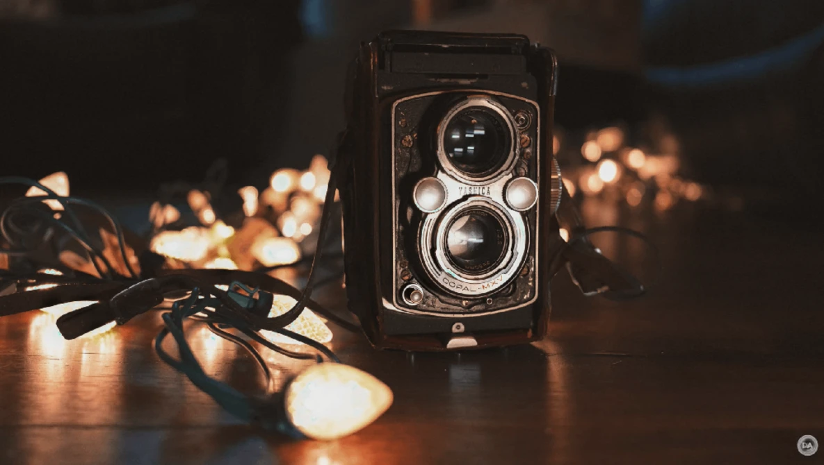 Vintage twin-lens reflex camera with attached cable release on wooden surface surrounded by warm bokeh lights.