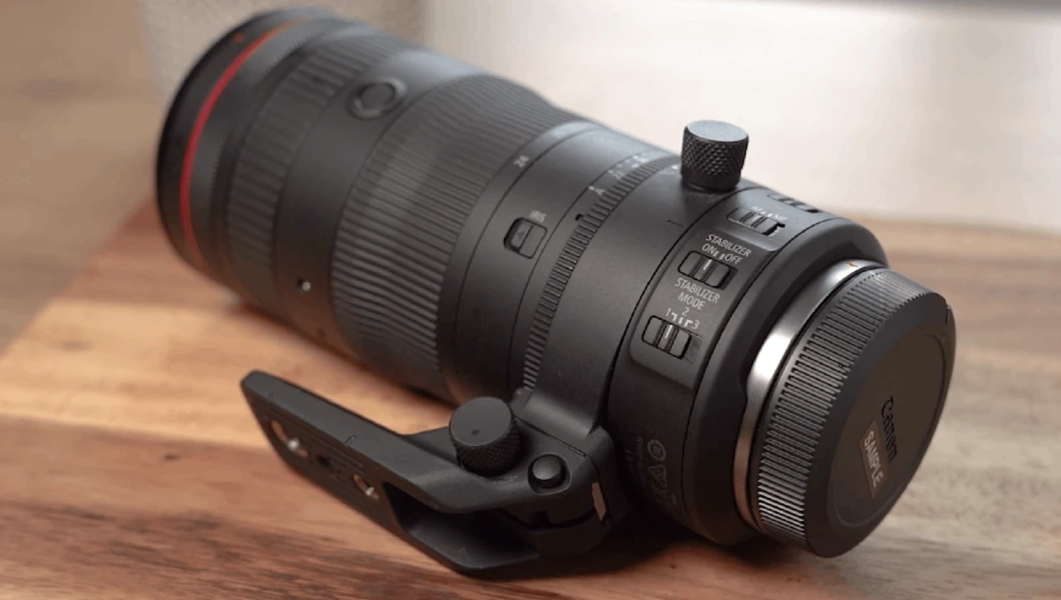 Black telephoto lens with red ring mounted on wooden surface with black camera strap.