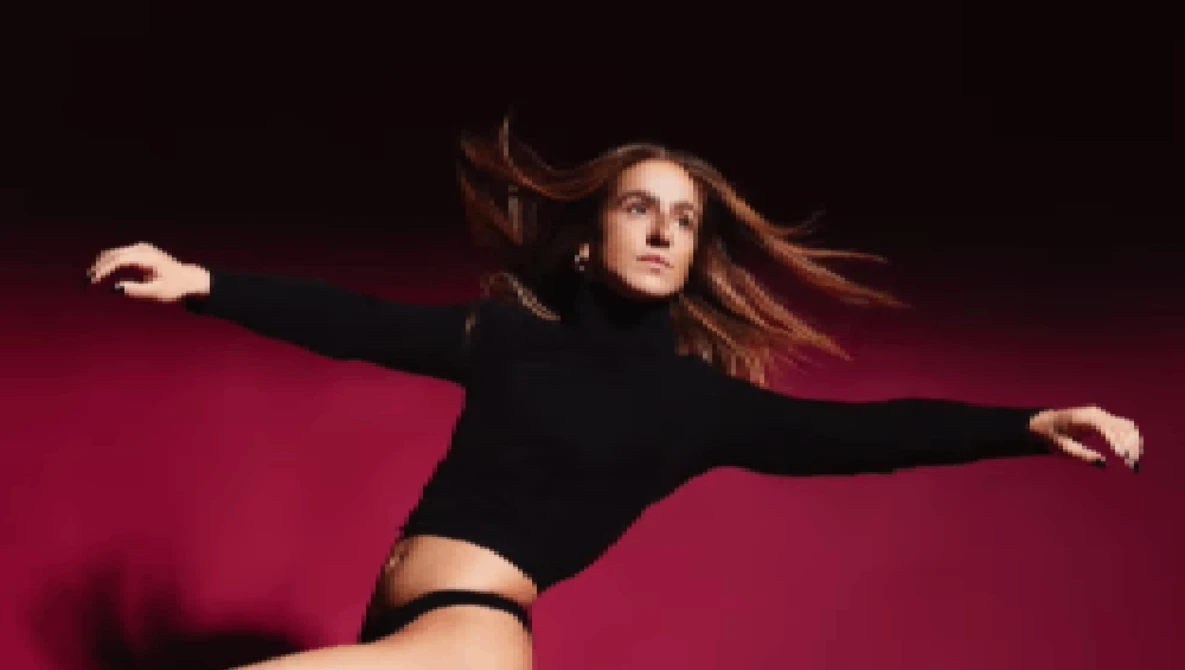 Woman in black crop top and high-waisted bottoms posed dynamically against deep magenta background with arms extended.