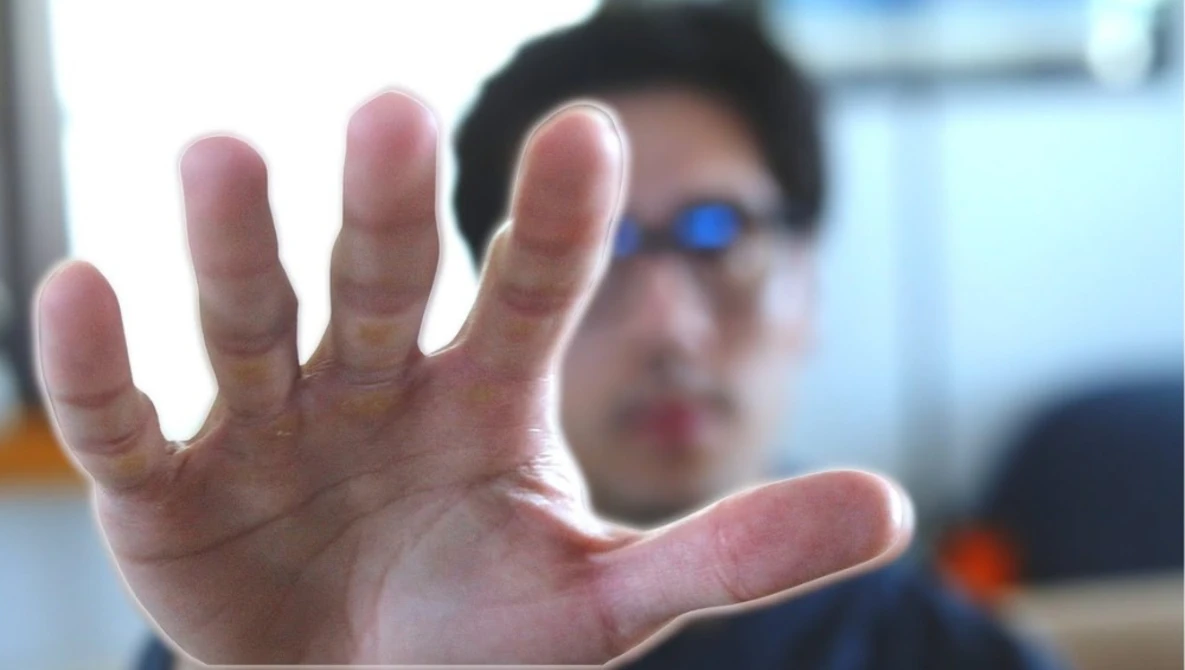 Person's open hand raised toward camera in close-up shot with blurred background.