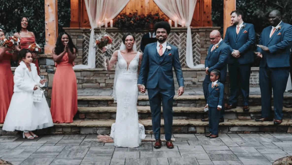 Bride and groom standing together during outdoor wedding ceremony with guests gathered behind them.