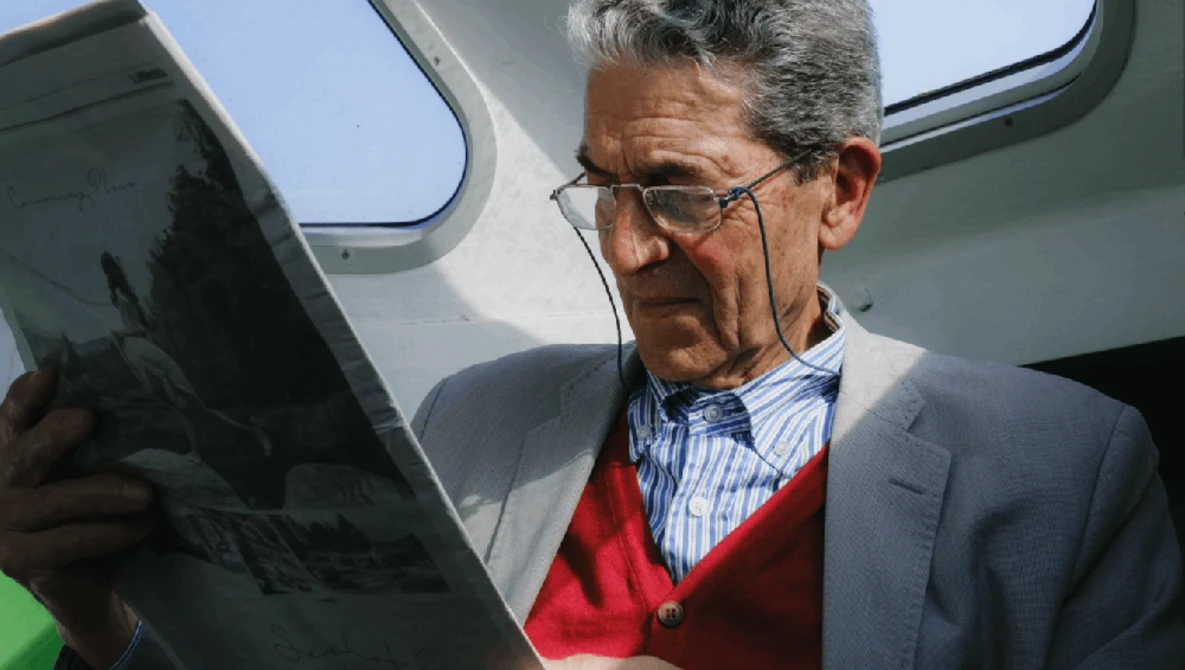 Man in blazer and red cardigan reviewing tablet outdoors near aircraft.