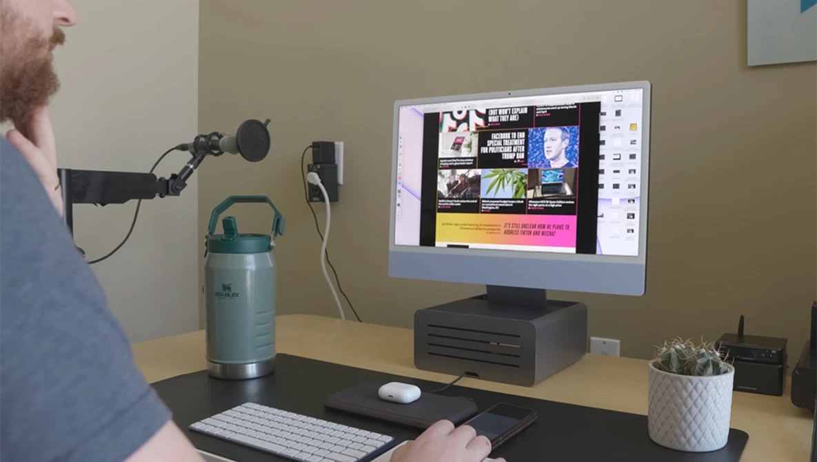 Podcaster or content creator speaking into a microphone at a desk setup with monitor displaying editing software.