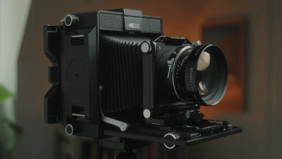 Vintage large format camera with bellows, mounted on tripod head with rangefinder lens attached.
