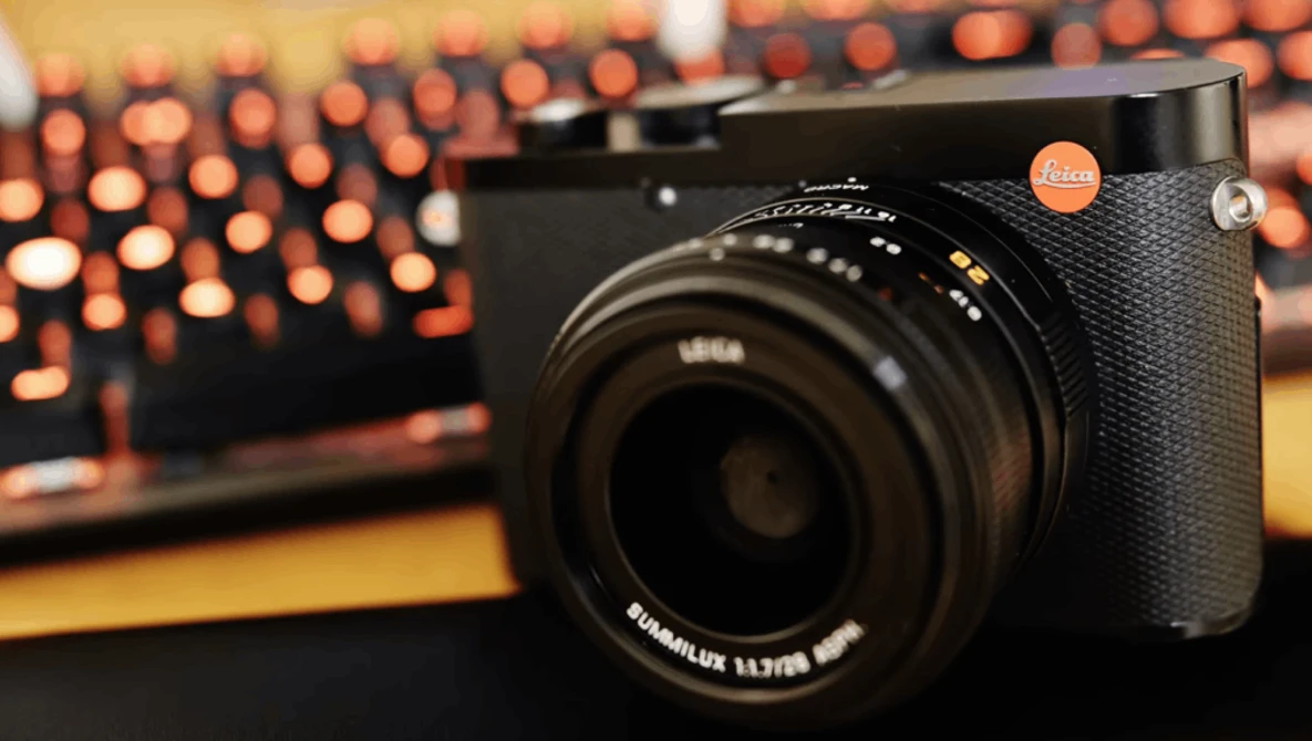 Leica Q2 camera with black leather grip and Summilux lens on wooden surface with blurred bokeh lights in background.