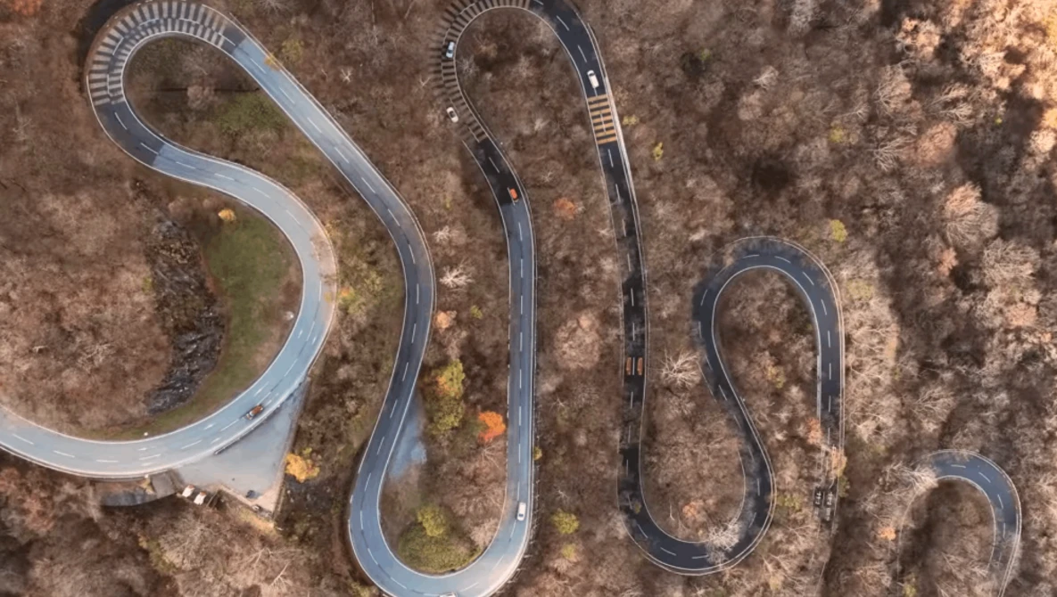 Aerial view of winding mountain roads cutting through forested terrain in serpentine patterns.