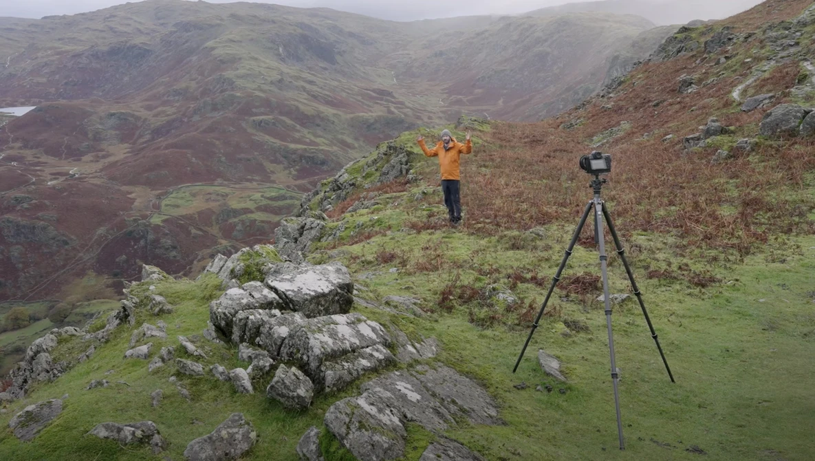Surveyor with theodolite on tripod in mountainous valley landscape.