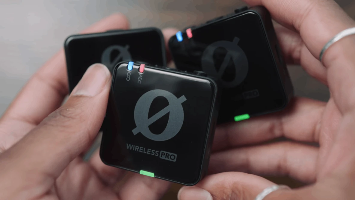 Three compact wireless audio transmitter units held in hands, displaying illuminated status indicators and branded logos.