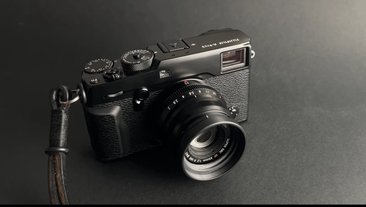 Black rangefinder camera with leather strap on dark gray background.