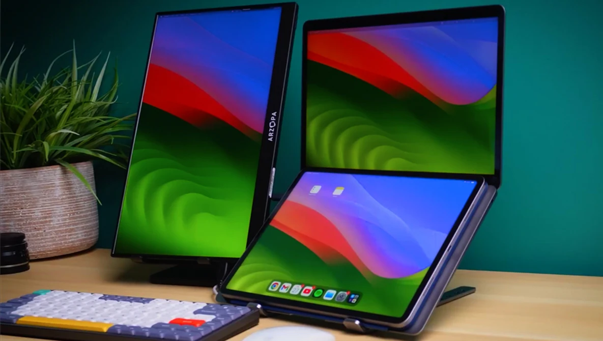Three foldable tablet devices displaying colorful gradient wallpapers on a wooden desk with a potted plant and keyboard nearby.