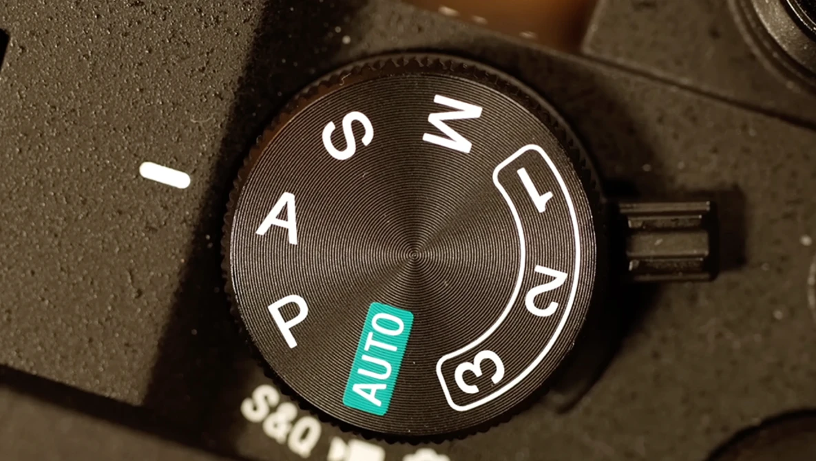 Close-up of a camera mode dial showing P, A, S, M, and AUTO settings with the dial positioned on AUTO.