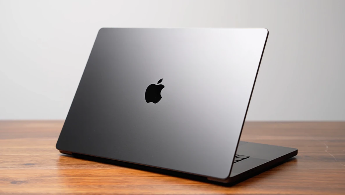 Space gray MacBook Pro closed on wooden surface against neutral background.