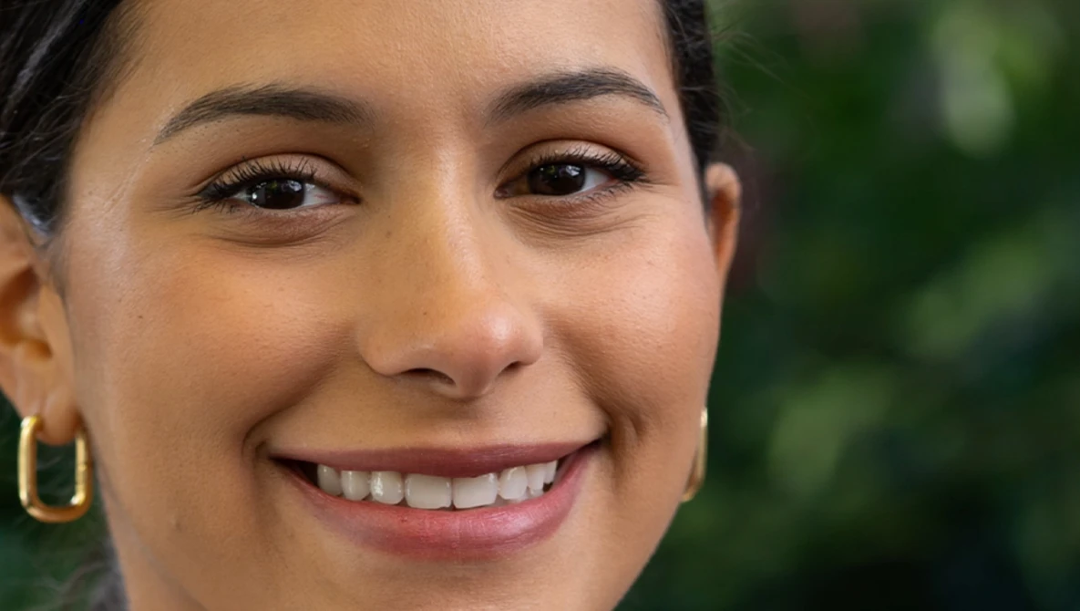 Close-up portrait of a woman smiling at the camera with natural outdoor lighting.