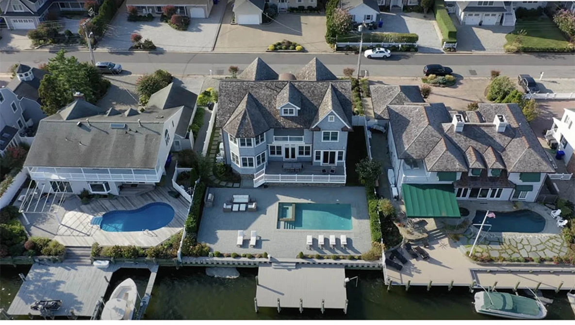 Aerial view of waterfront homes with pools and docks along a residential canal.