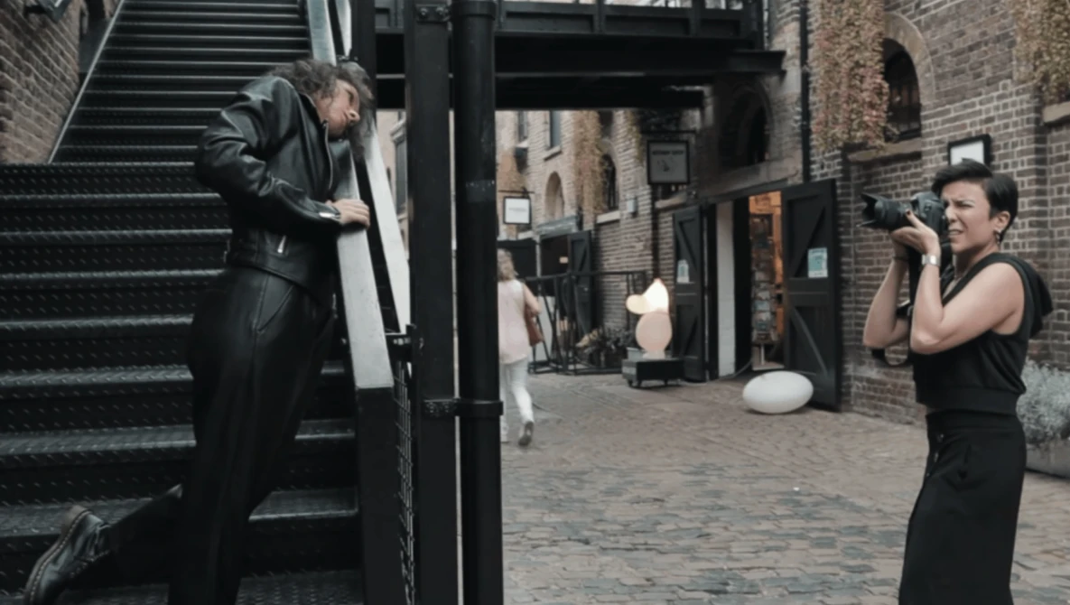 Fashion photographer shooting a model on urban brick alleyway steps.