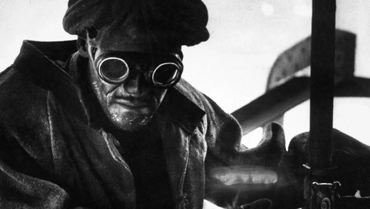 Black and white portrait of a person wearing circular goggles and dark clothing, shot from a low angle.