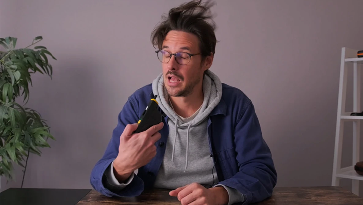 Man in glasses holding a dark bottle while speaking animatedly at a table.